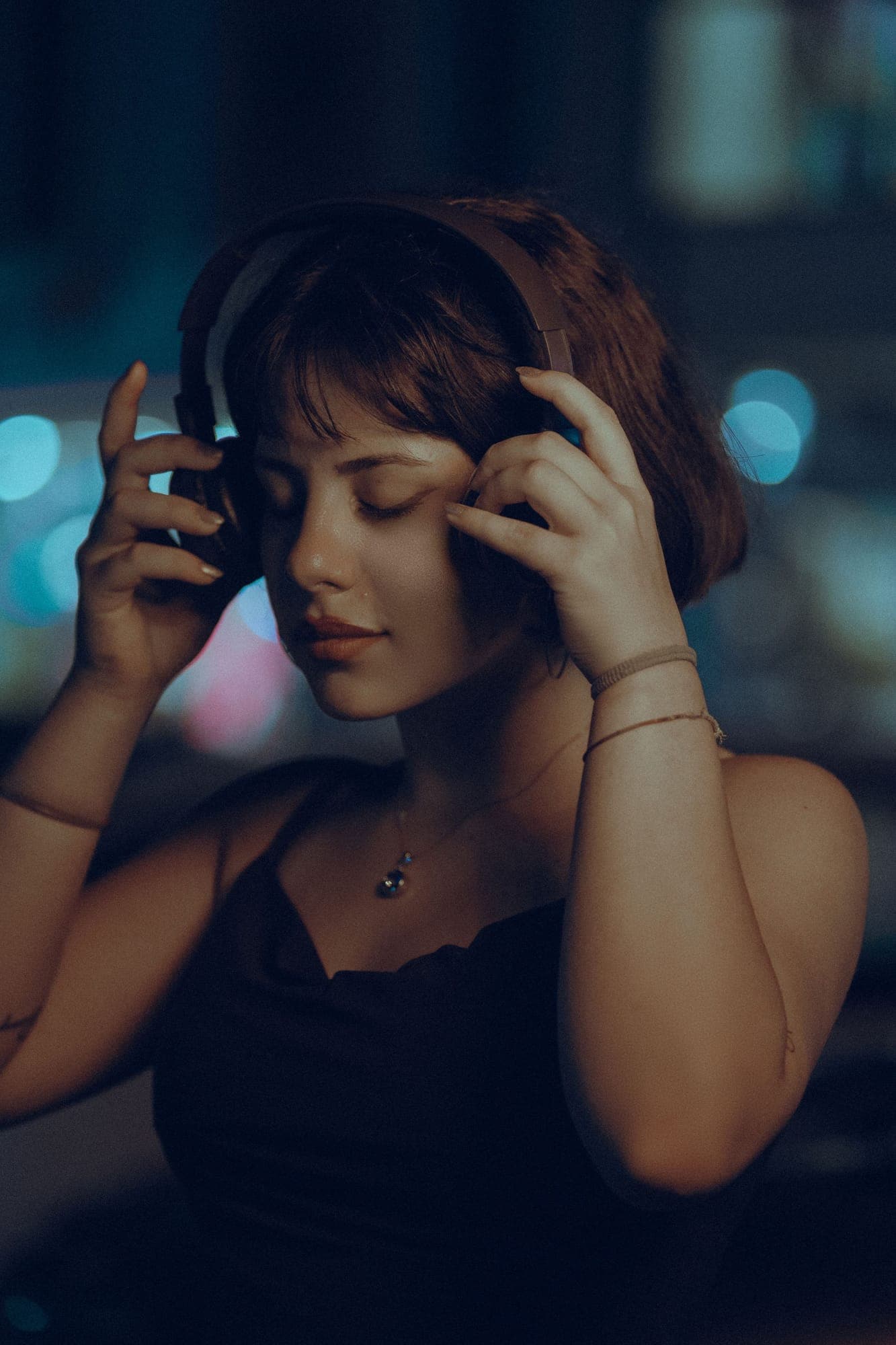 A woman with headphones listening with her eyes closed under city lights