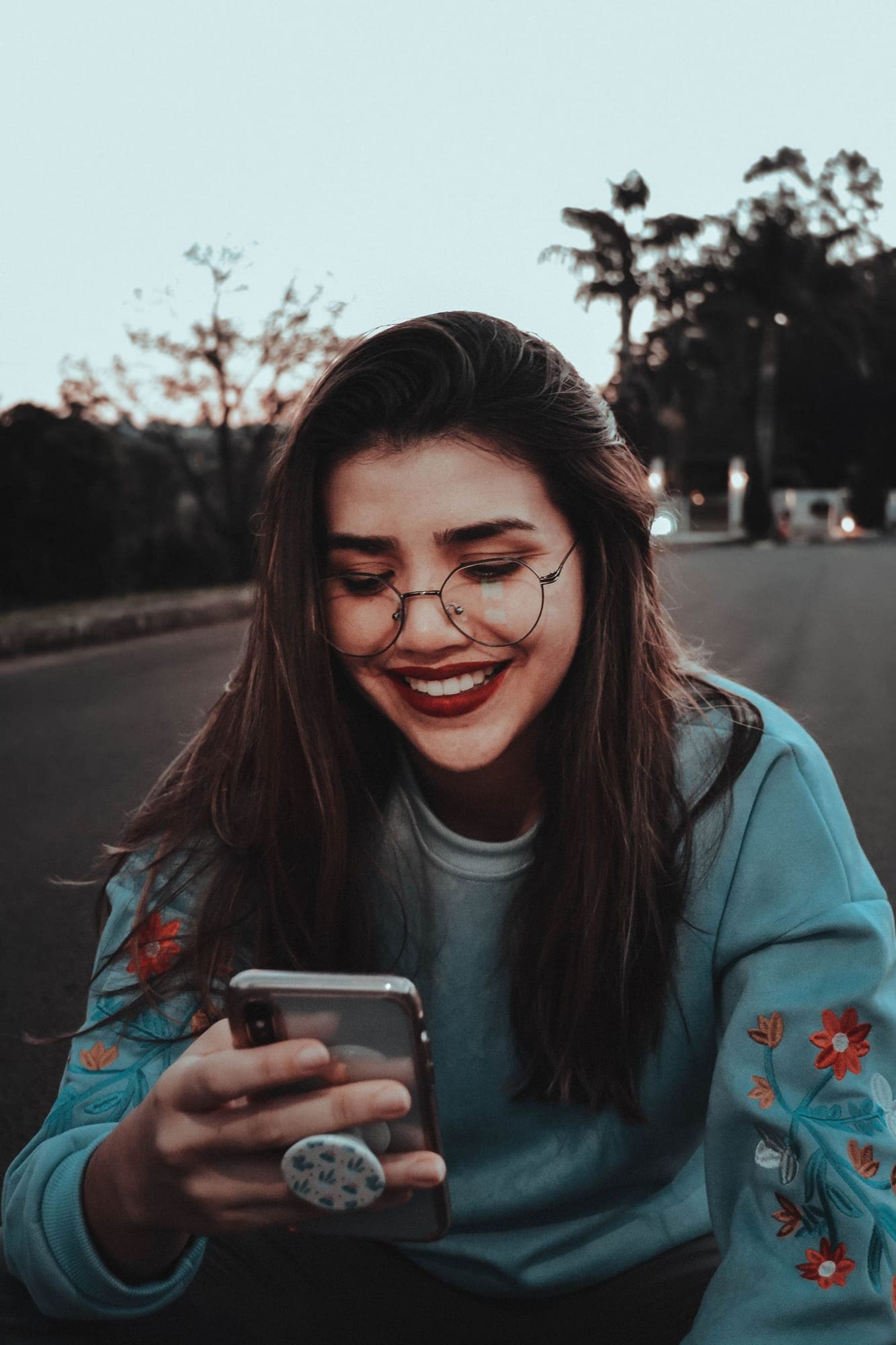 A young woman smiling at her phone on an evening street